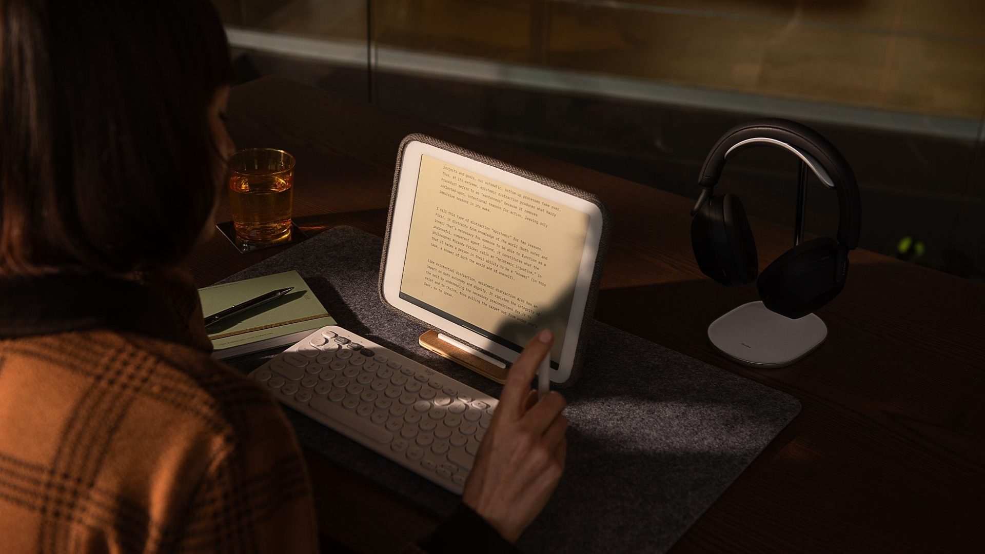 A person taps on the Daylight Computer tablet, with a wireless keyboard in front of it. The room is dark and the tablet is illuminated by its screen.