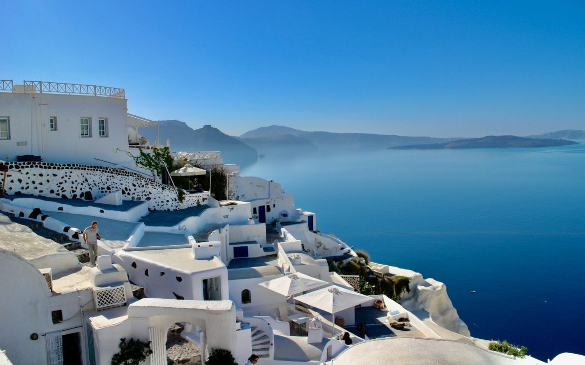 An aerial view over the sea, mountains and white-washed rooftops in Greece.
