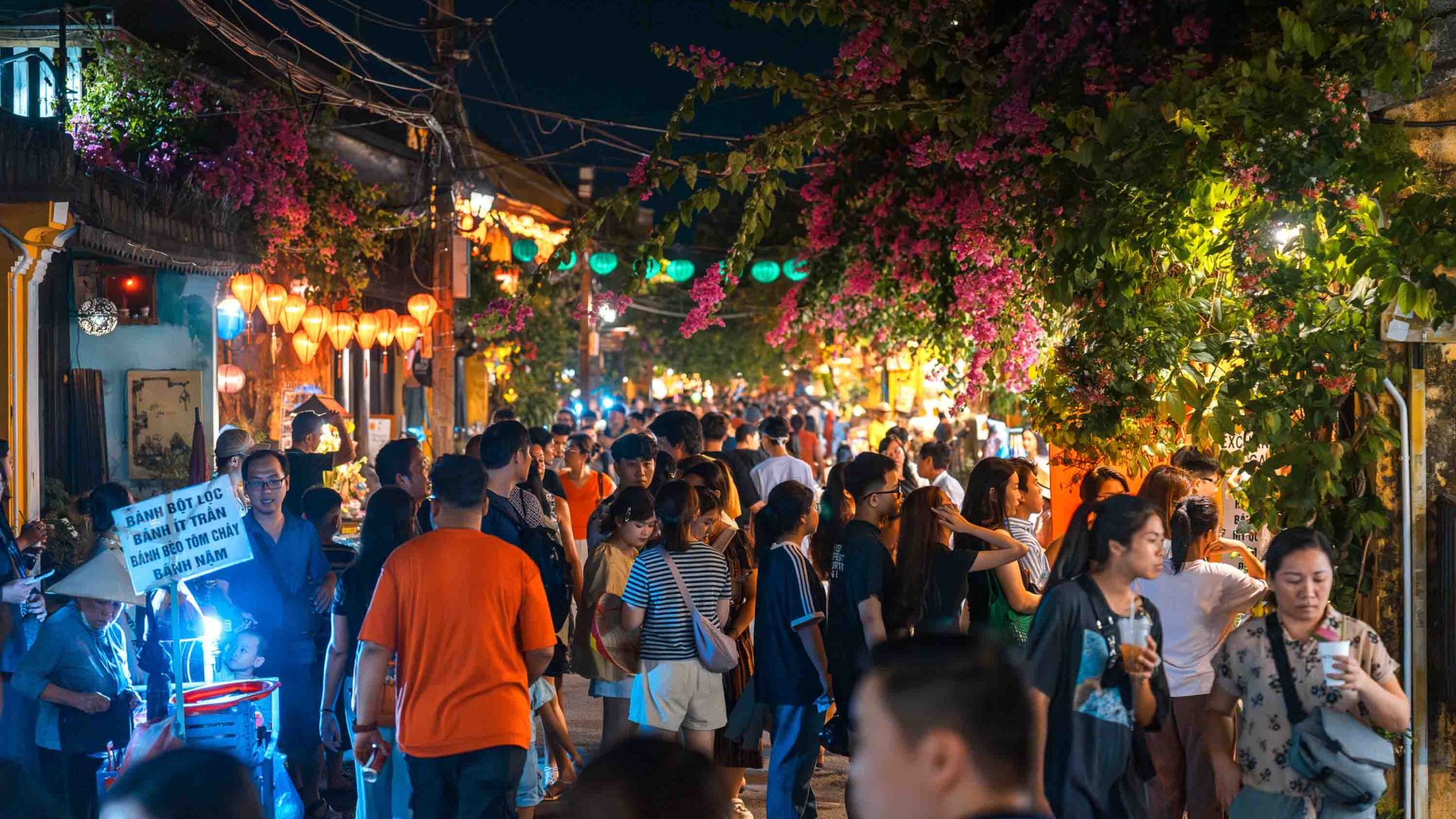 Tourists fill a street lined with lanterns at night.
