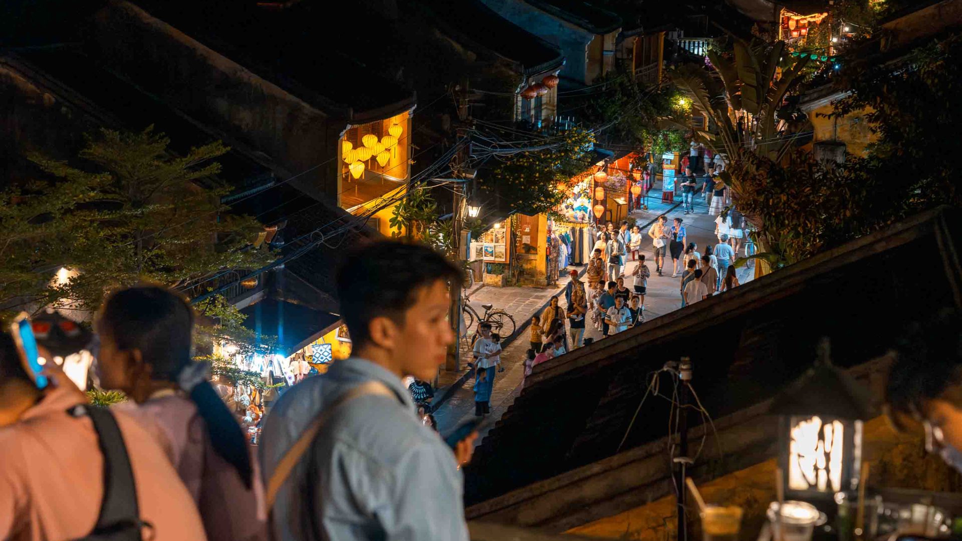 Tourists fill a street lined with lanterns at night.