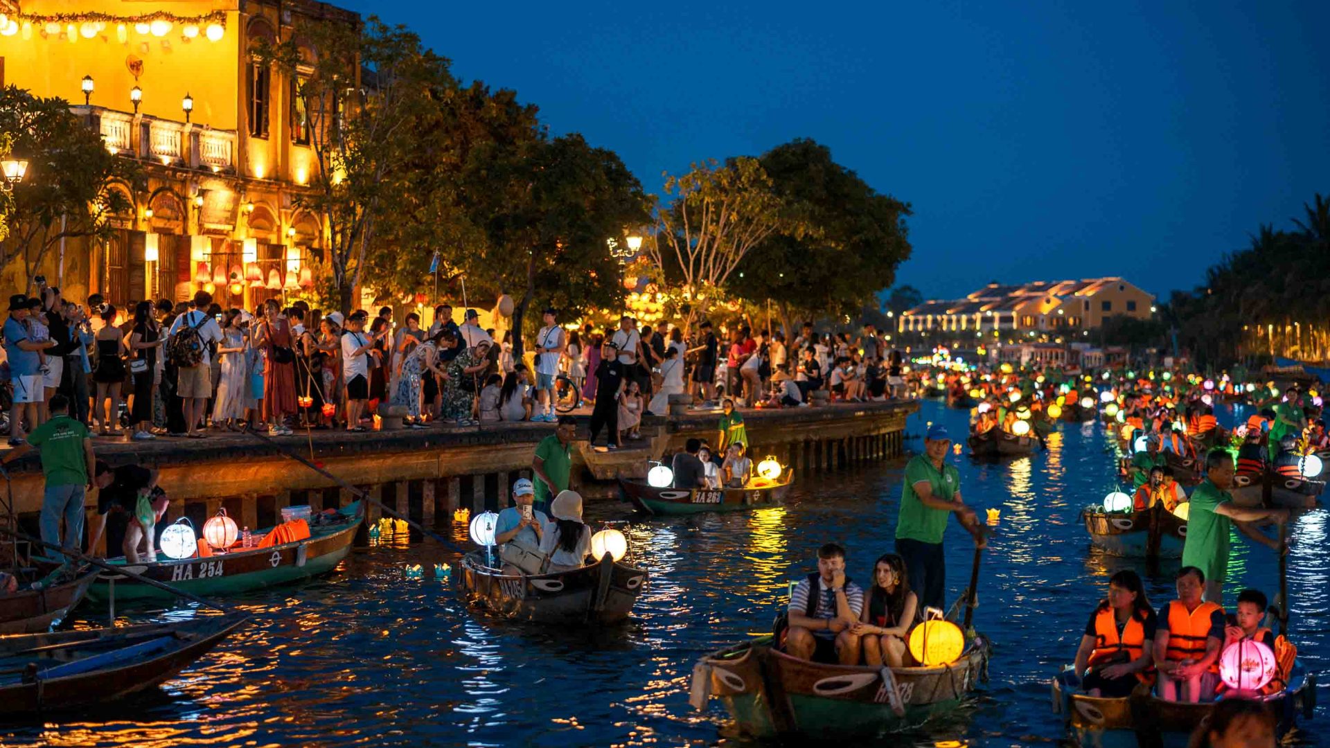 Streets and the canal are crowded with tourists, lit by lanterns.
