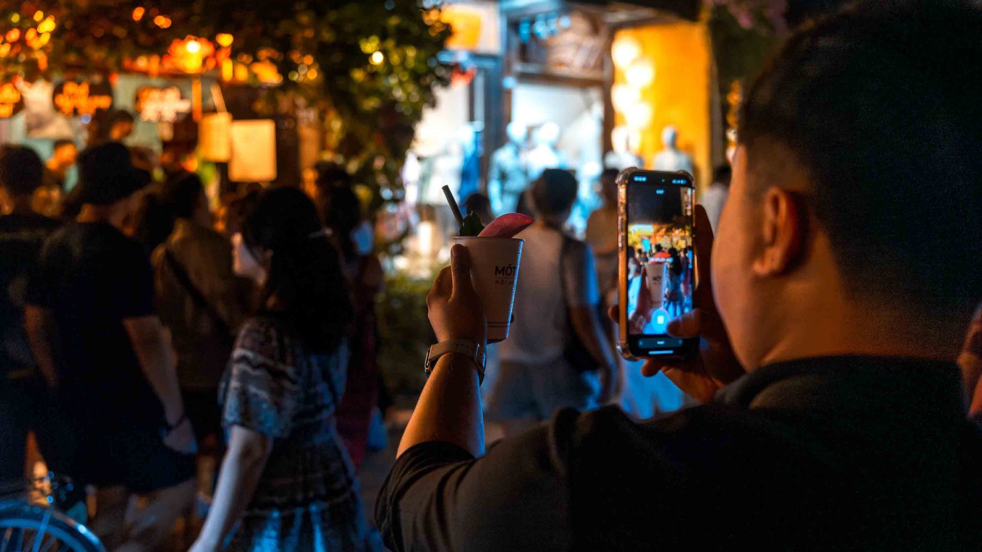 A man takes a photo of his cup of Mót tea in front of the busy shop.