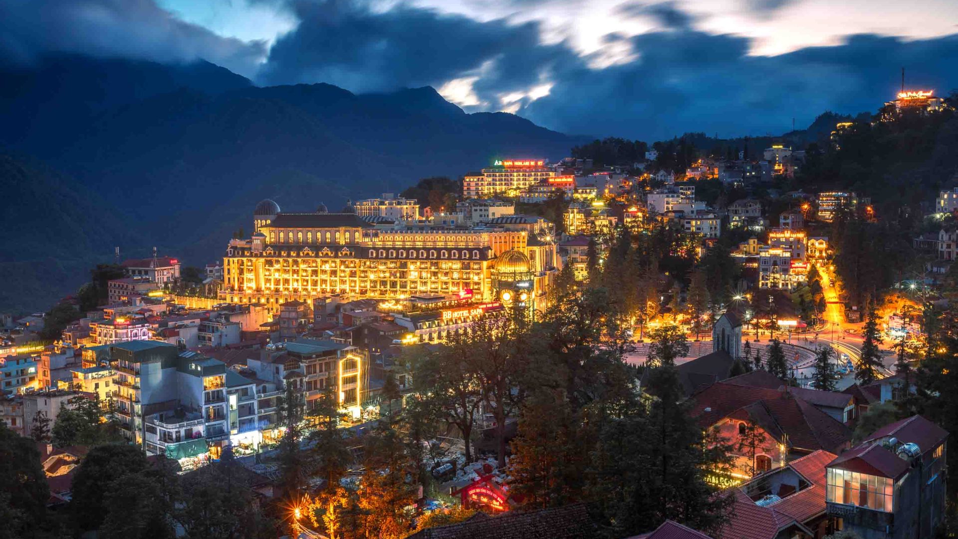 A town in the mountains is lit up brightly at night, and has lots of hotels and other buildings.