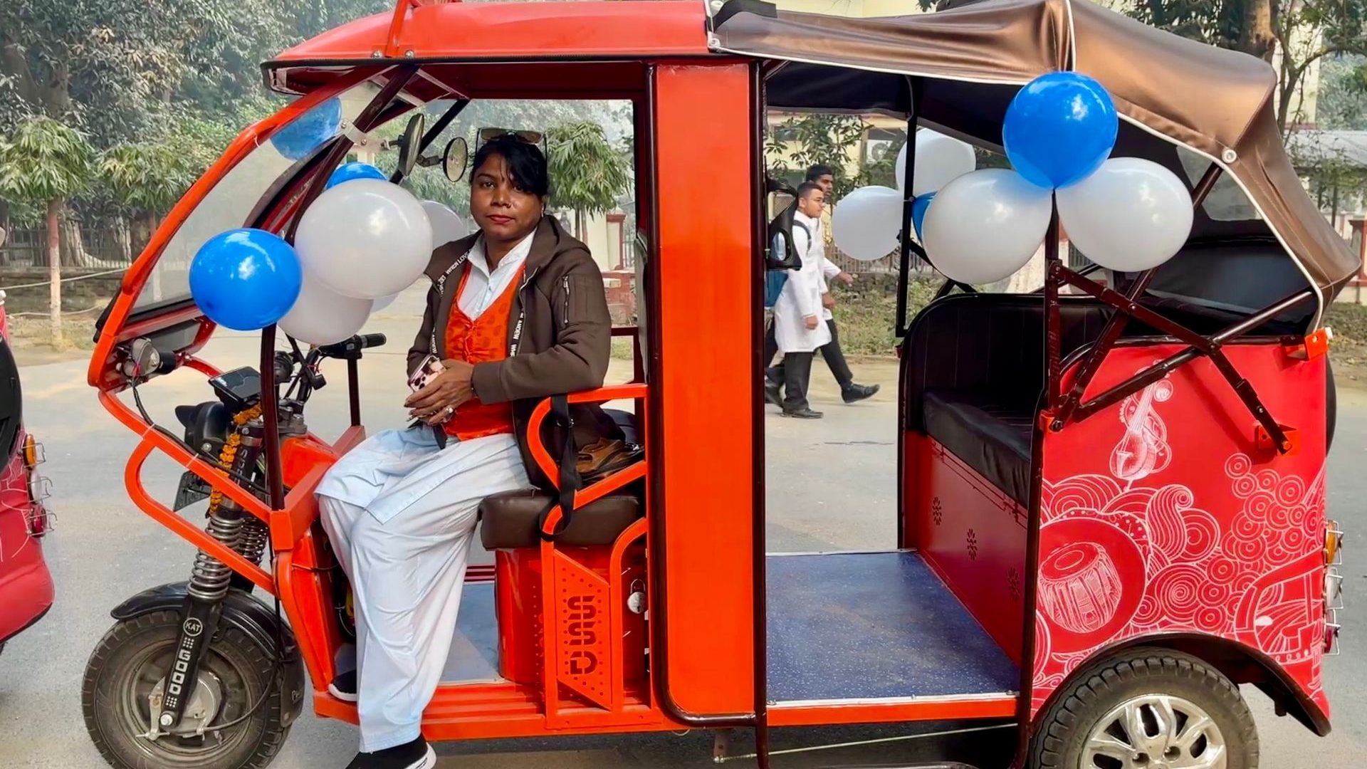 A woman stands beside a red electric rickshaw.