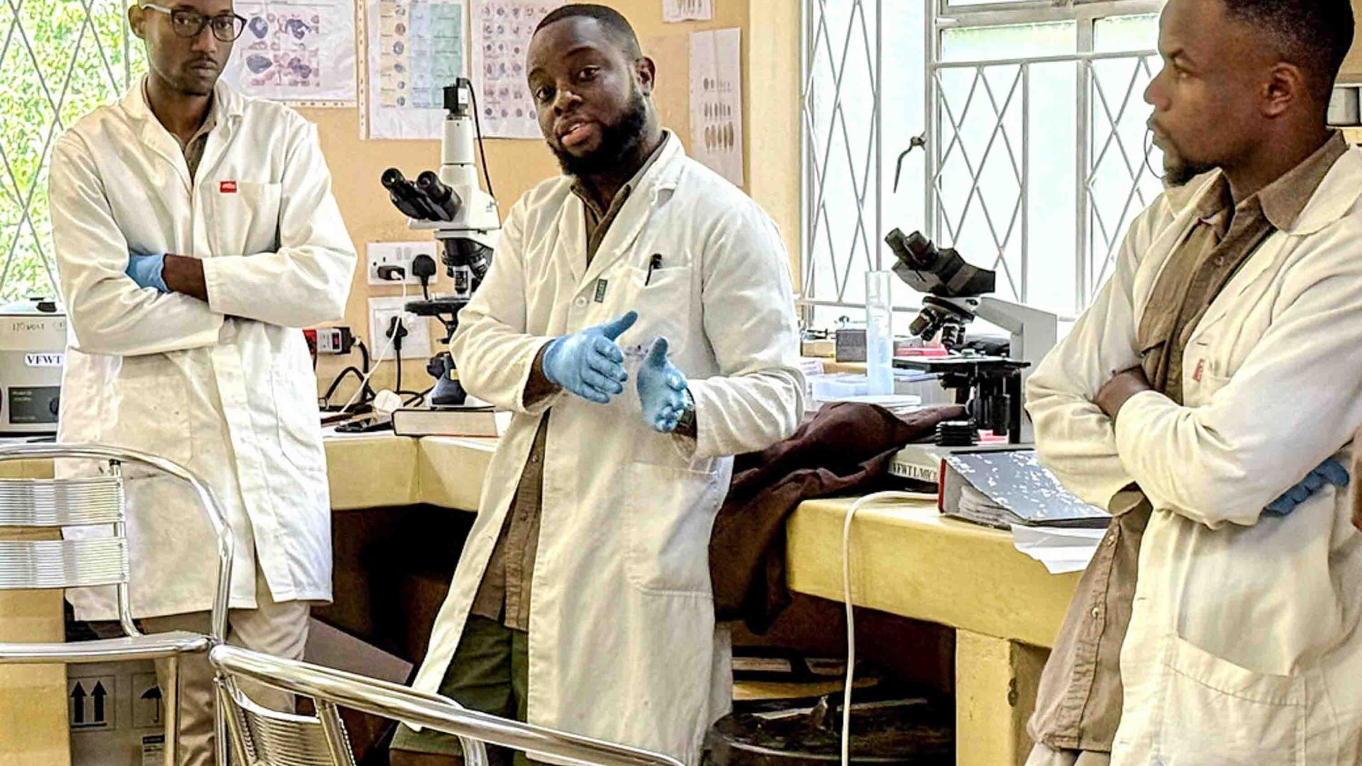 Three scientists in lab coats in a lab are talking.