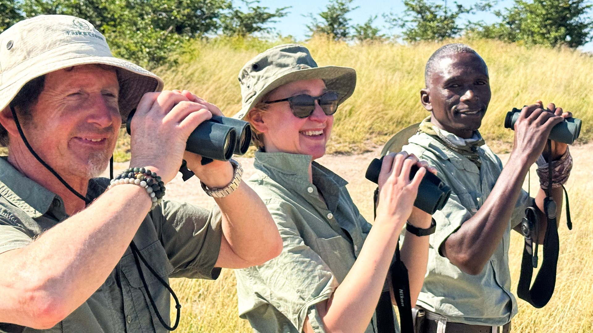 Three people smile as they hold binoculars.