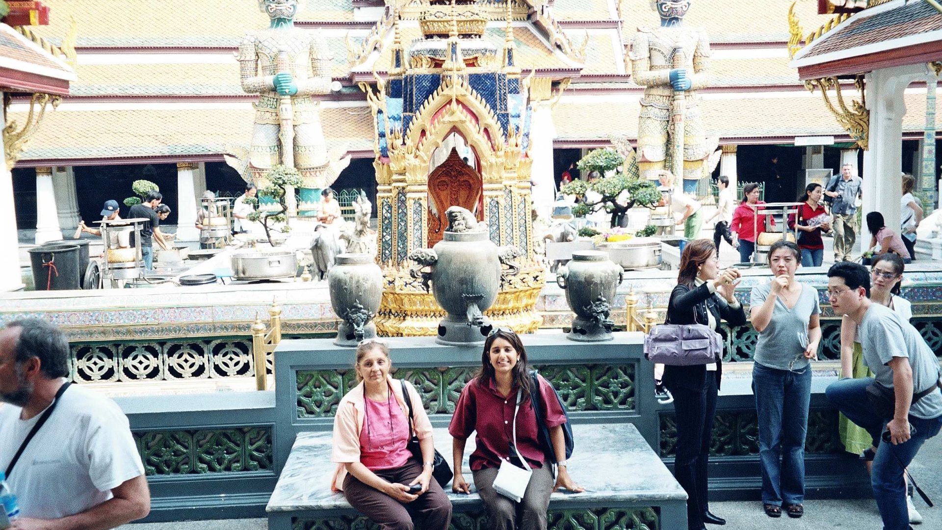 Two women sit on a bench with an ornate Buddhist temple behind them