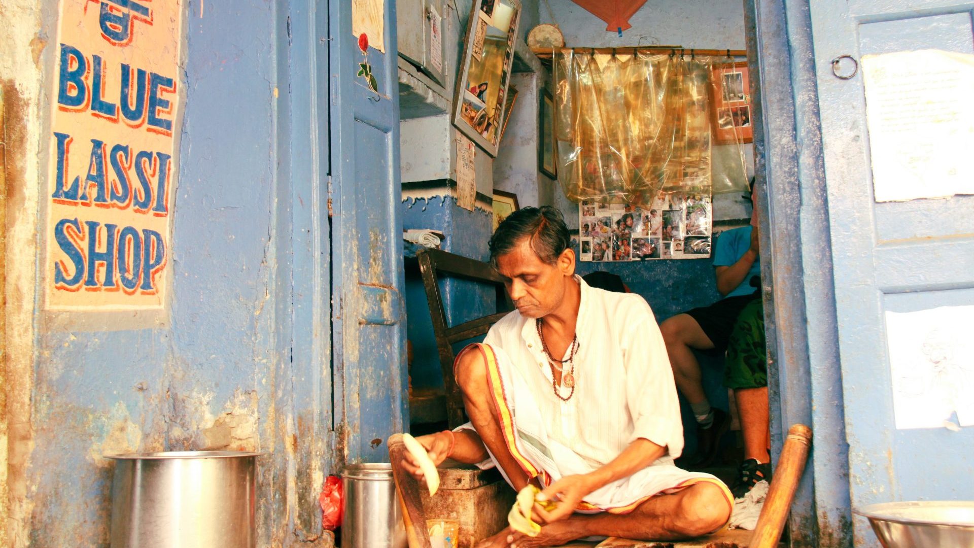 A man sits on the floor of his lassie (yogurt drink) shop, preparing drinks.