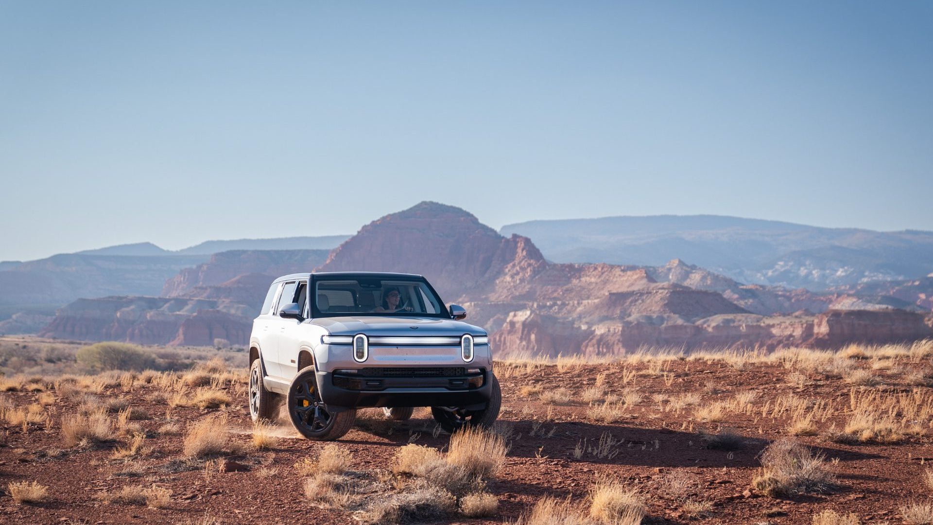 Silver electric vehicle drives across red rock landscape