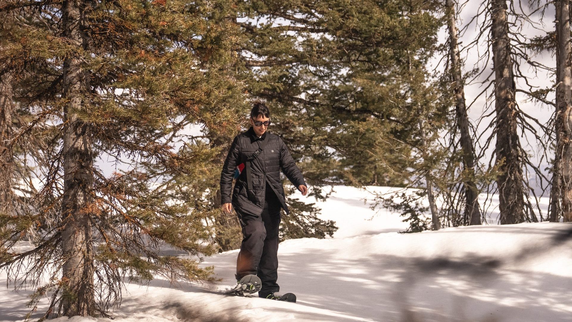 Woman snowshoes through snow beneath conifers