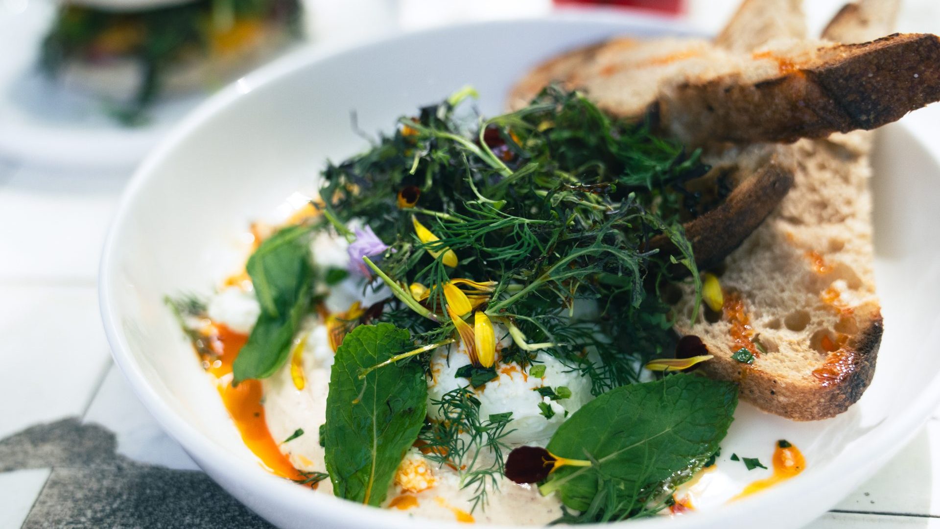 White bowl with eggs, fresh greens and edible flowers.