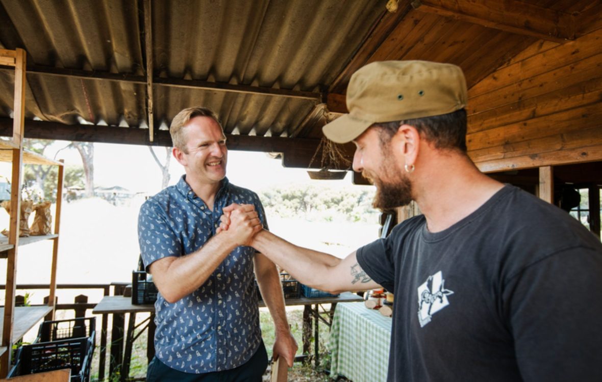 Two men smile and clasp hands