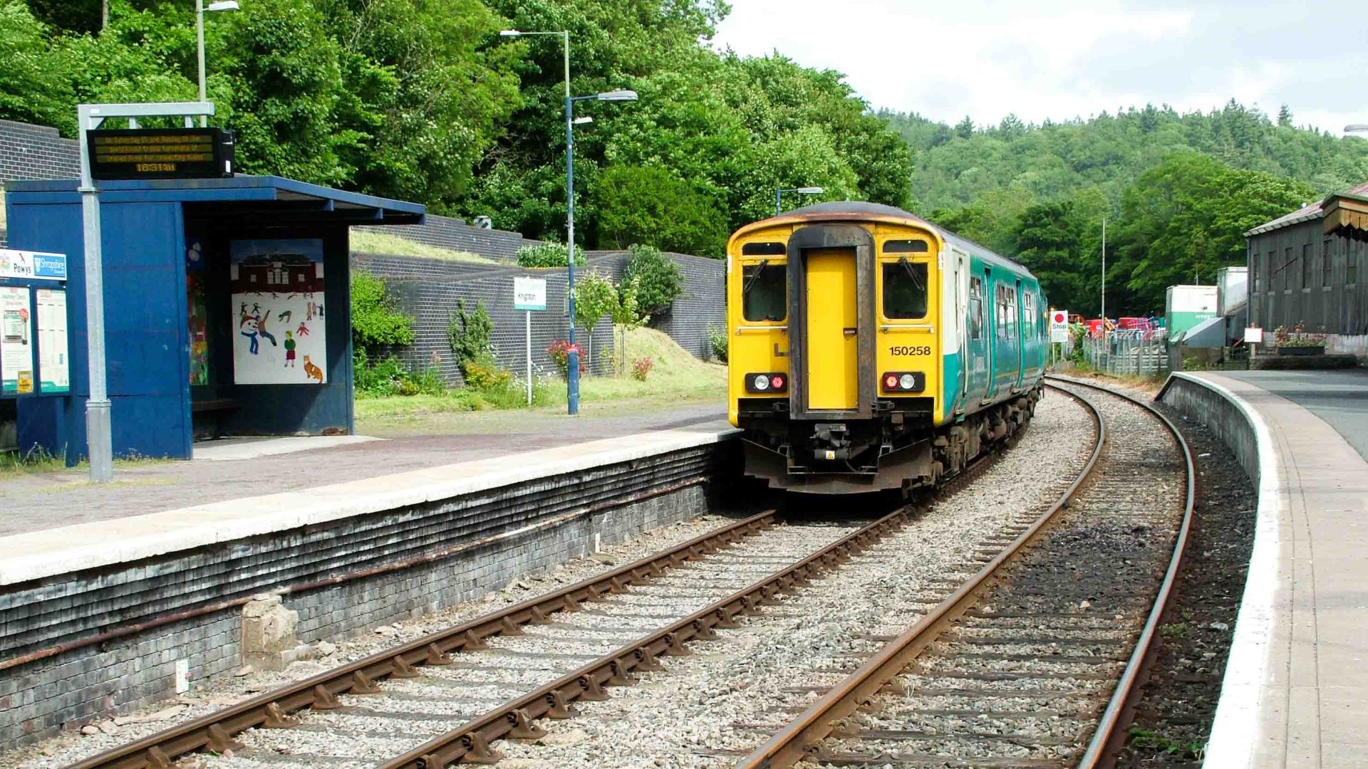 A yellow and green train is stopped at a train station.