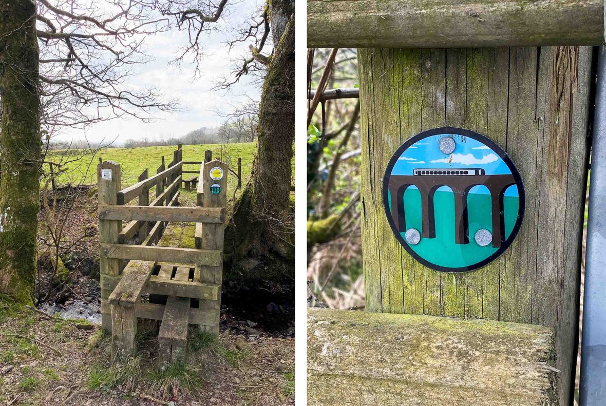 A wooden pedestrian bridge and a sign which has an illustration of a train crossing a viaduct.