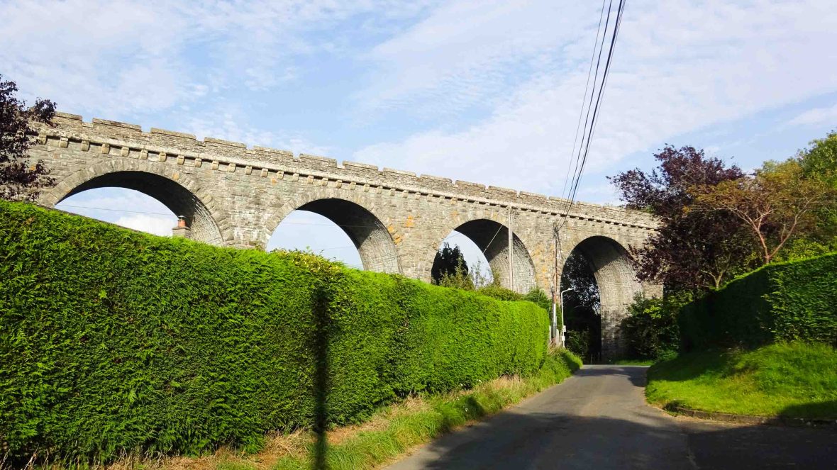 A viaduct made of stone crosses above a road.
