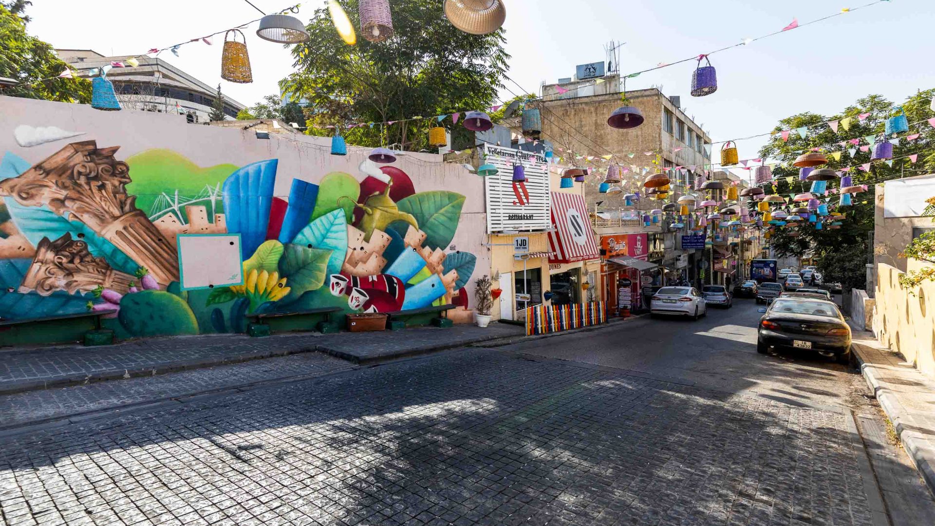A street with street art on the walls and colourful baskets hanging from wires above the street.