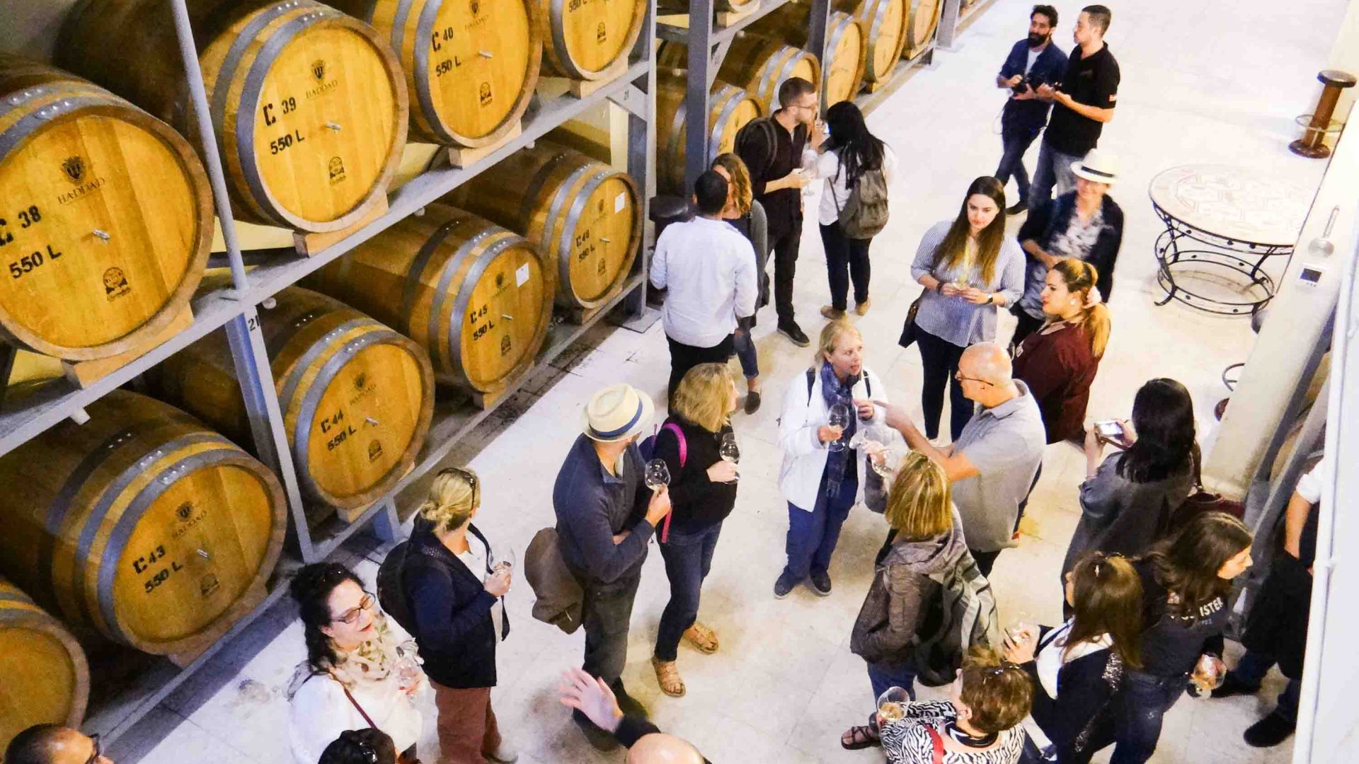 People sample wine alongside rows of barrels.