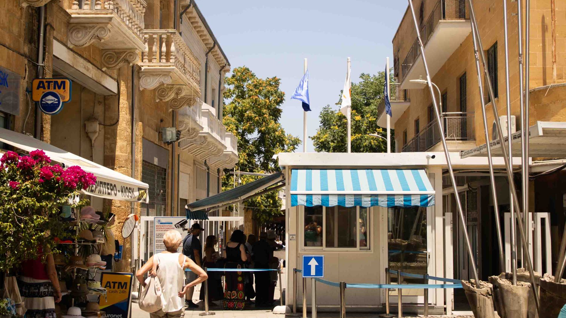 A checkpoint with a striped awning and people walking past it.