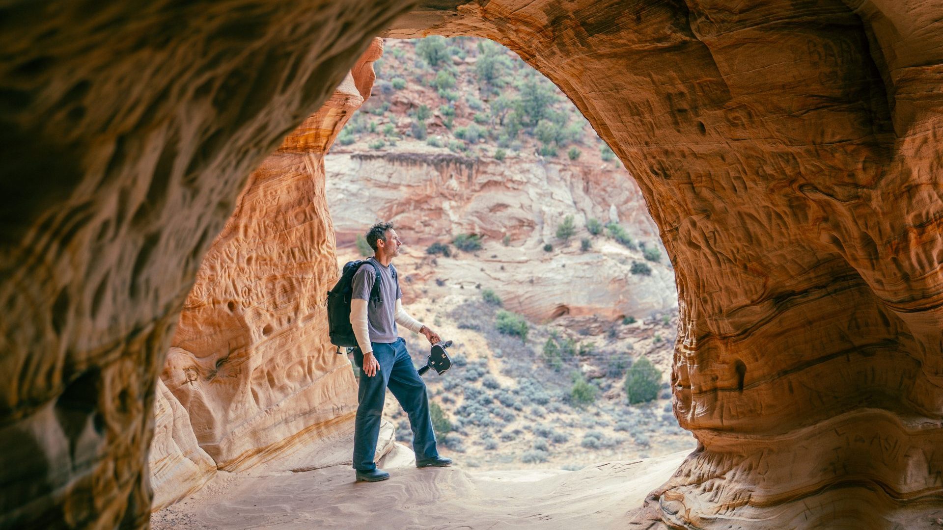 Man stands in the mouth of a red rock cave