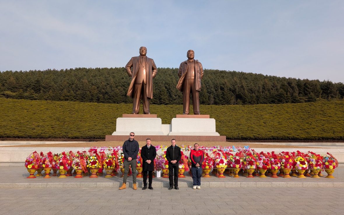 Four white Western men stand in a line in front of bronze statues