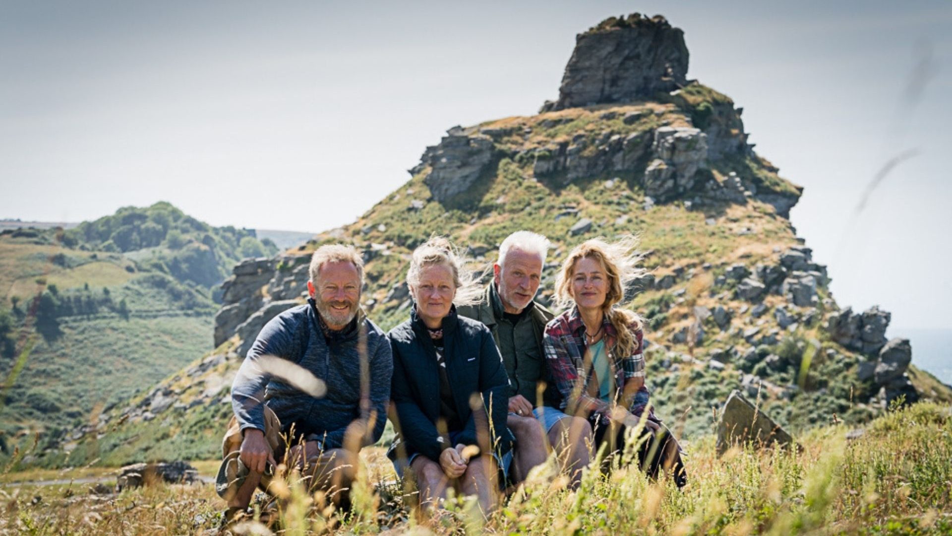Four people pose for a picture with a countryside backdrop during filming of a movie.
