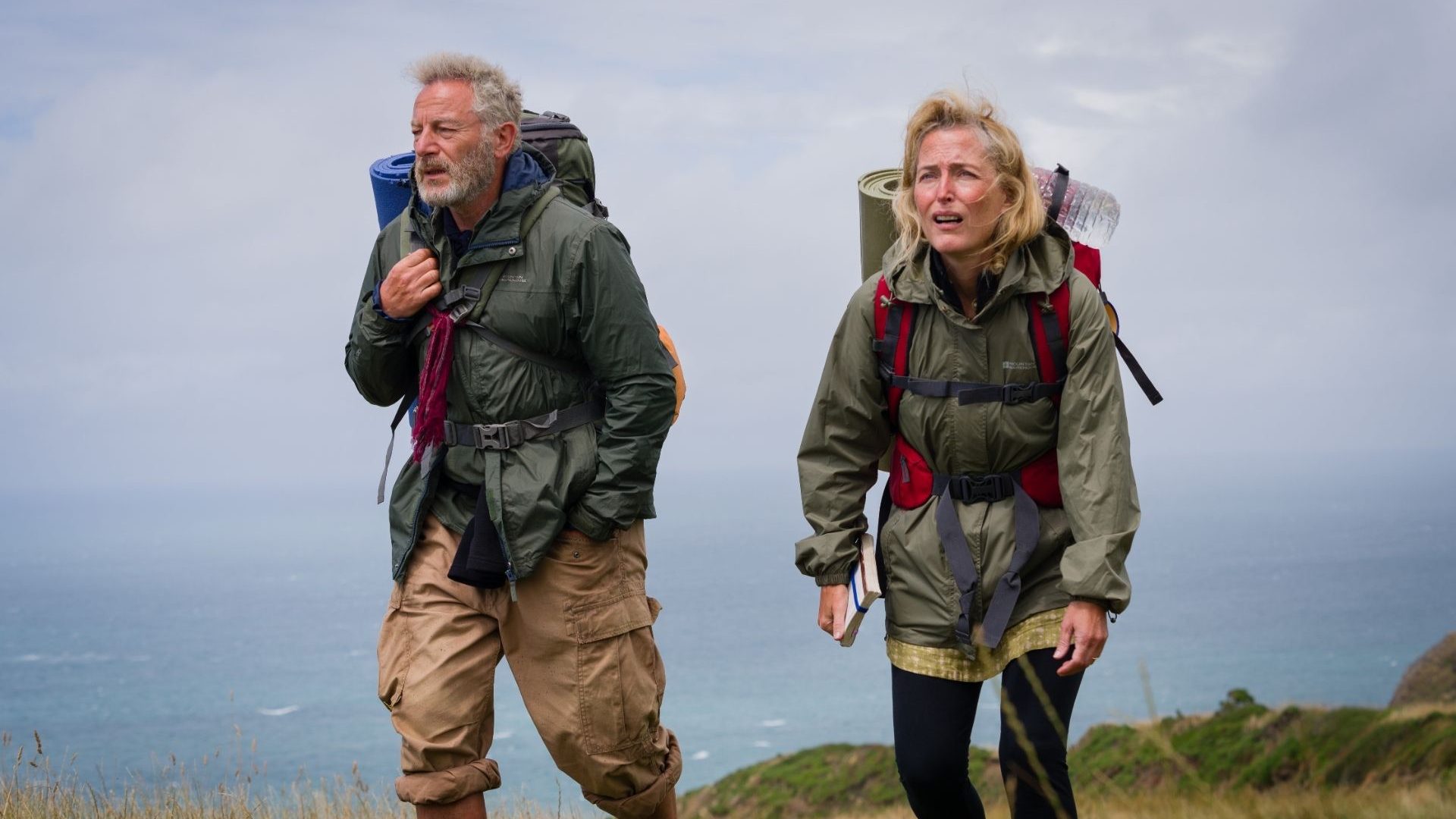 A man and woman in hiking gear walking along a clifftop.