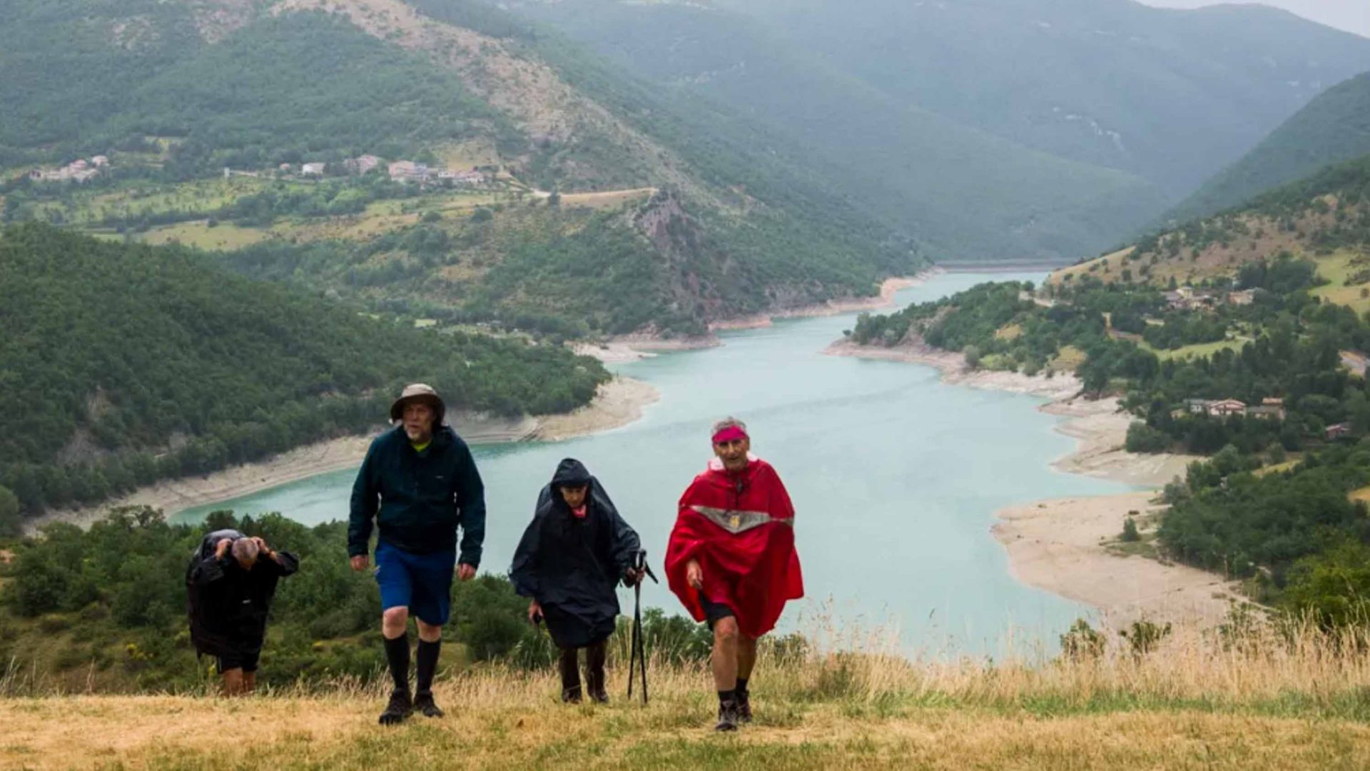 Three people hike up a hill from a lake below.