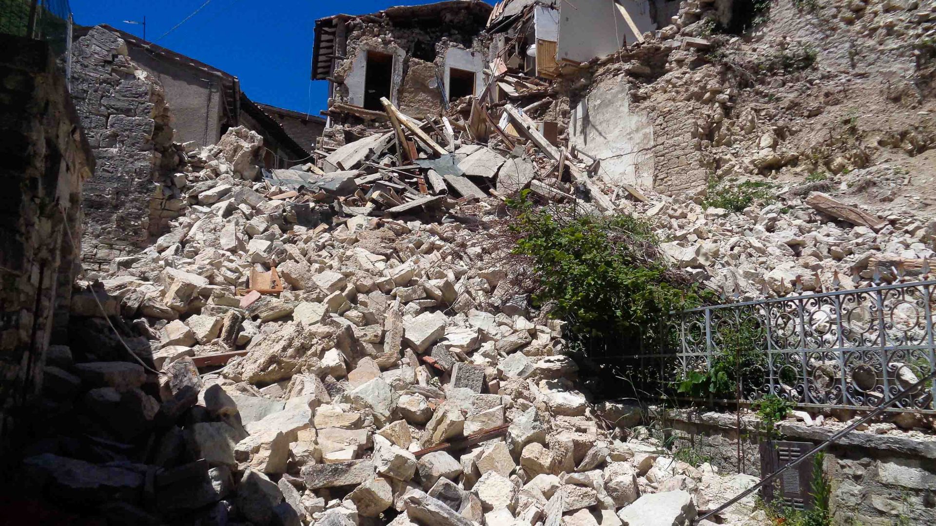 Bricks and rubble cascade down a hill from a house that also has damage.
