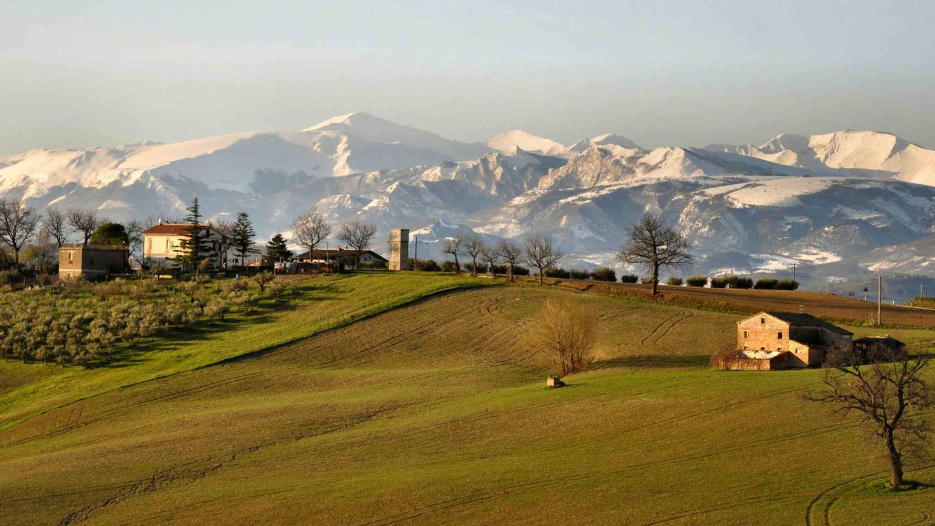 A few houses dot the hillsides. Snowy mountains are in the background.