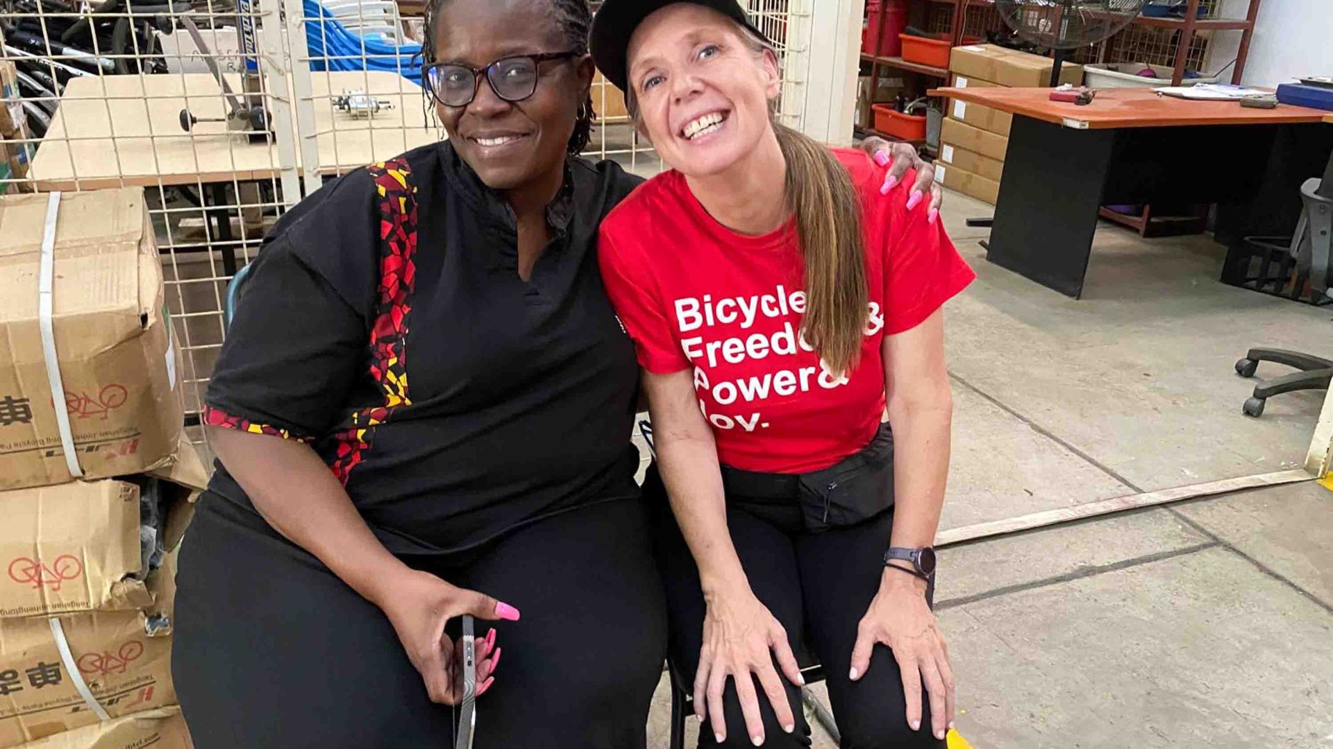 Two women sit sit by side and smile to camera.