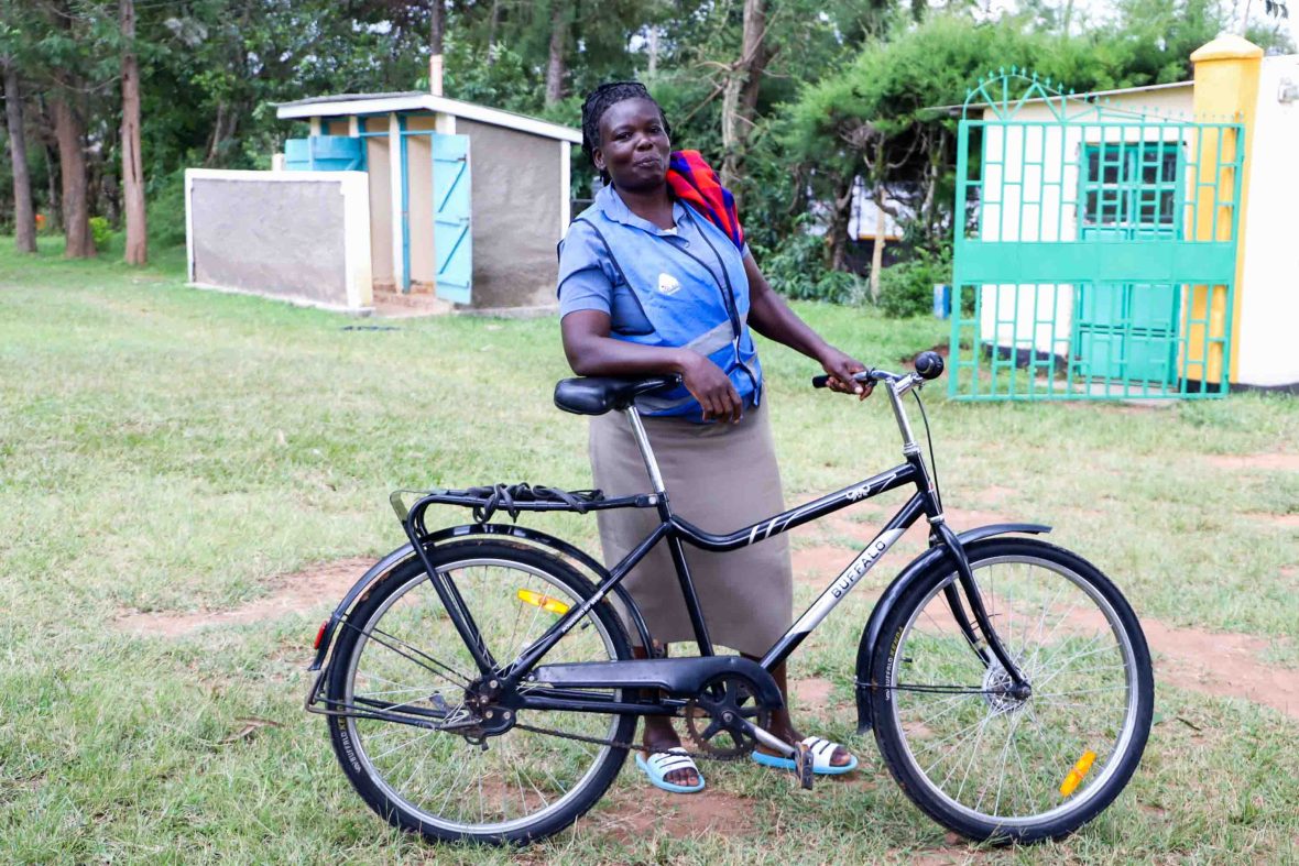 A woman in a blue shirt stands holding a bike outside a clinic building.