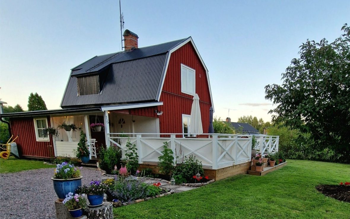 A red, barn-like house with white trim and a white fence, pictured at sunset.