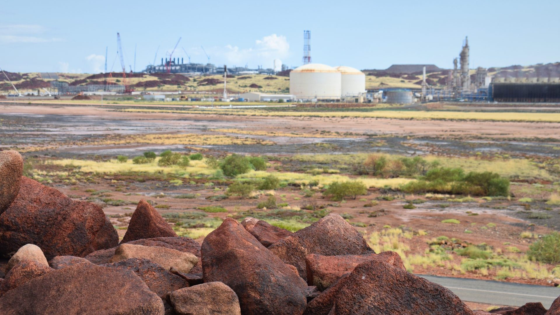 Red rock in the foreground, an oil and gas plant in the background