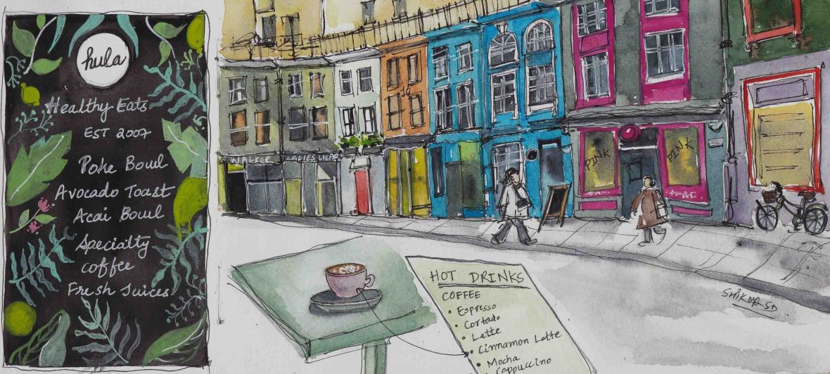 A cafe menu and a coffee on a table in a street lined with colourful buildings.