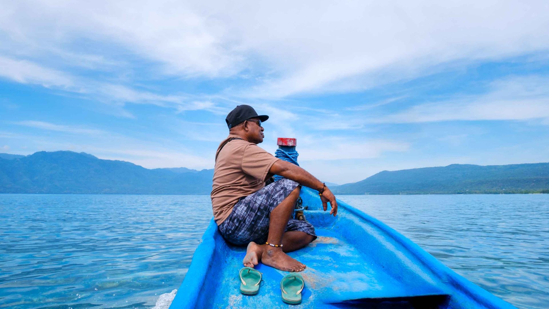 A man sits on the bow of a small boat looking out at the water.