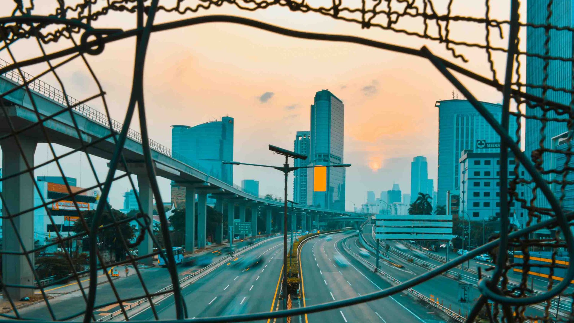 A city seen at sunset through some broken wire fencing.