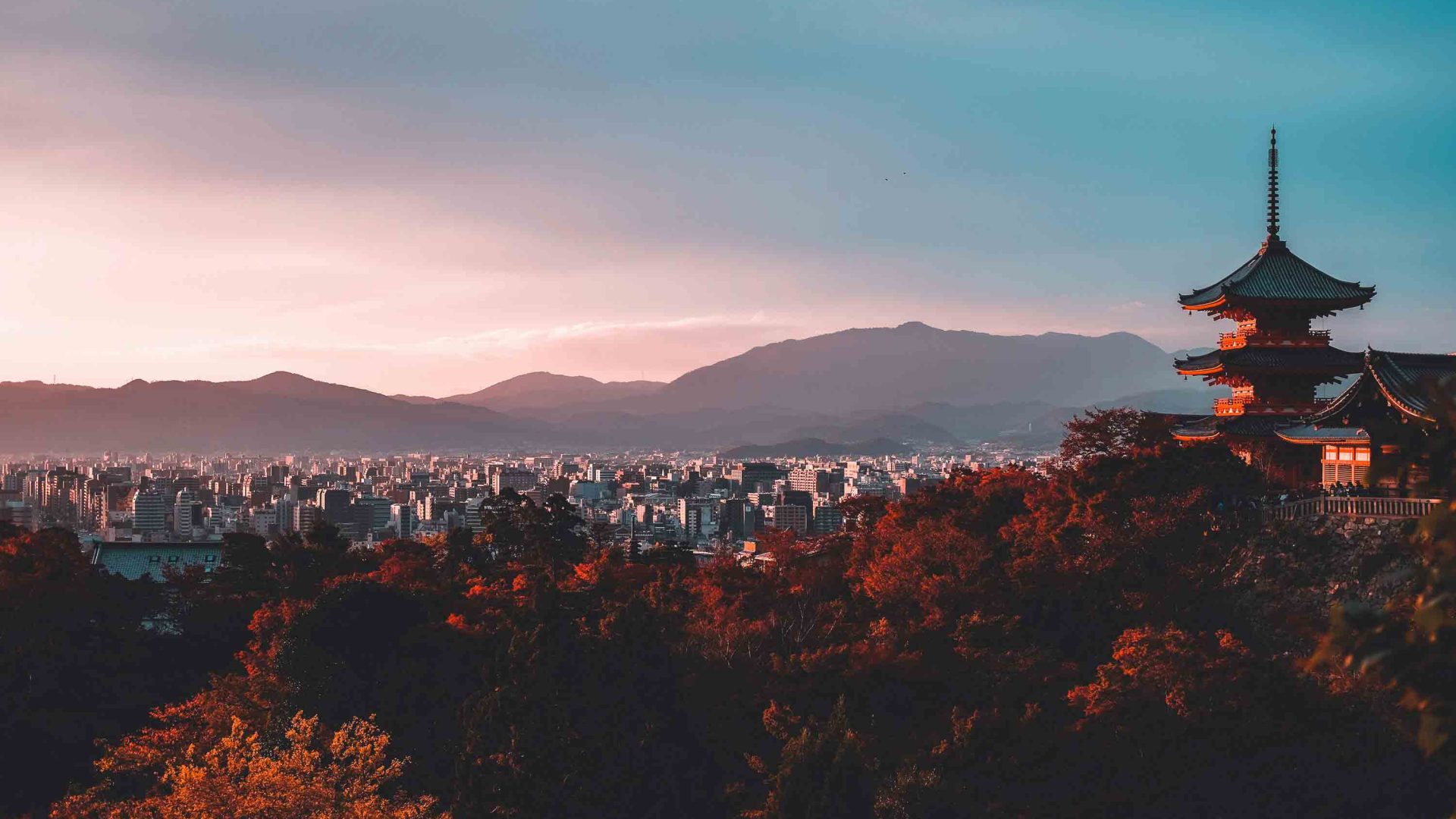 Kyoto in the distance in low light. Trees and a temple are i the foreground.