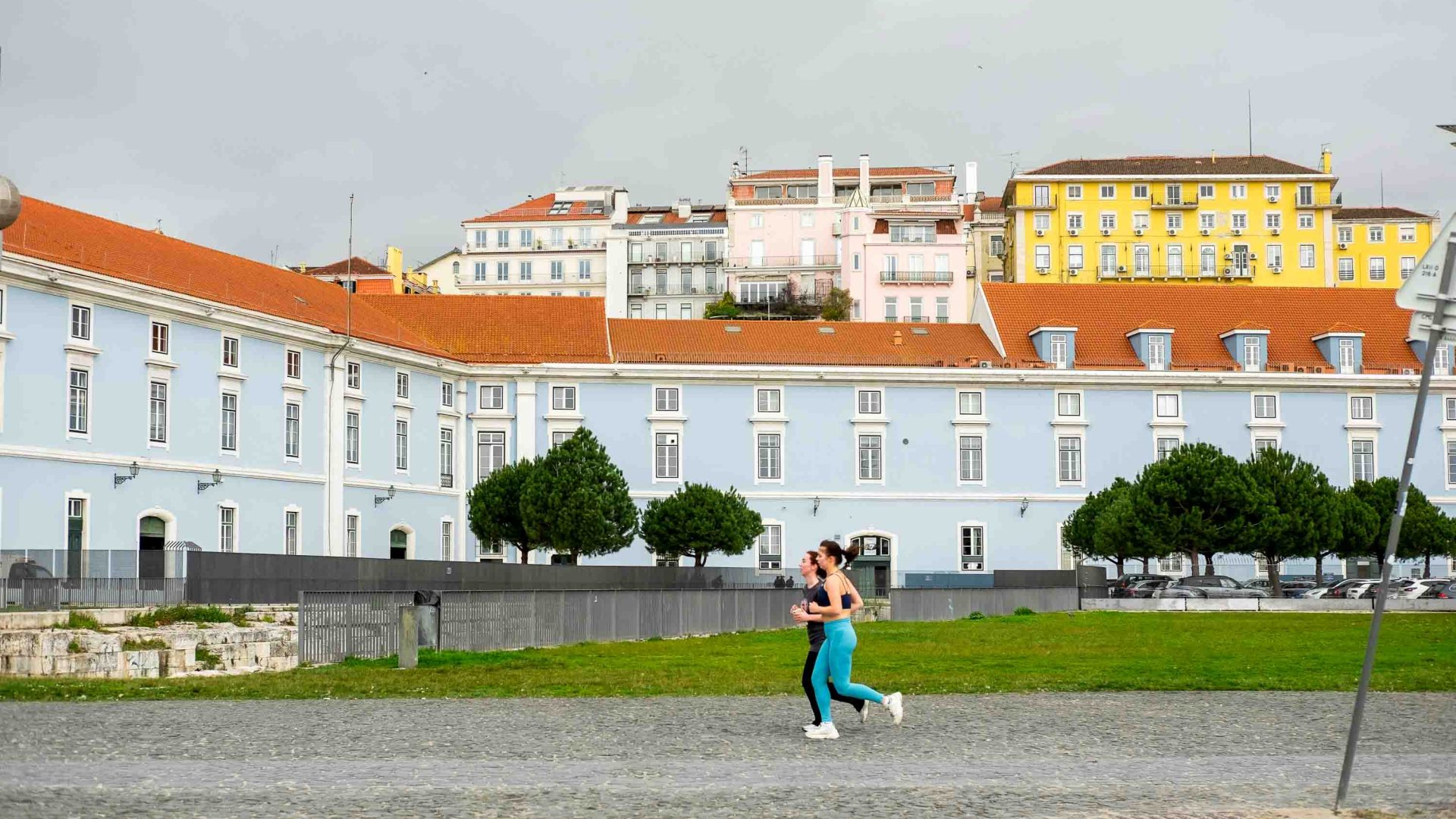 Two women run past colourful buildings.