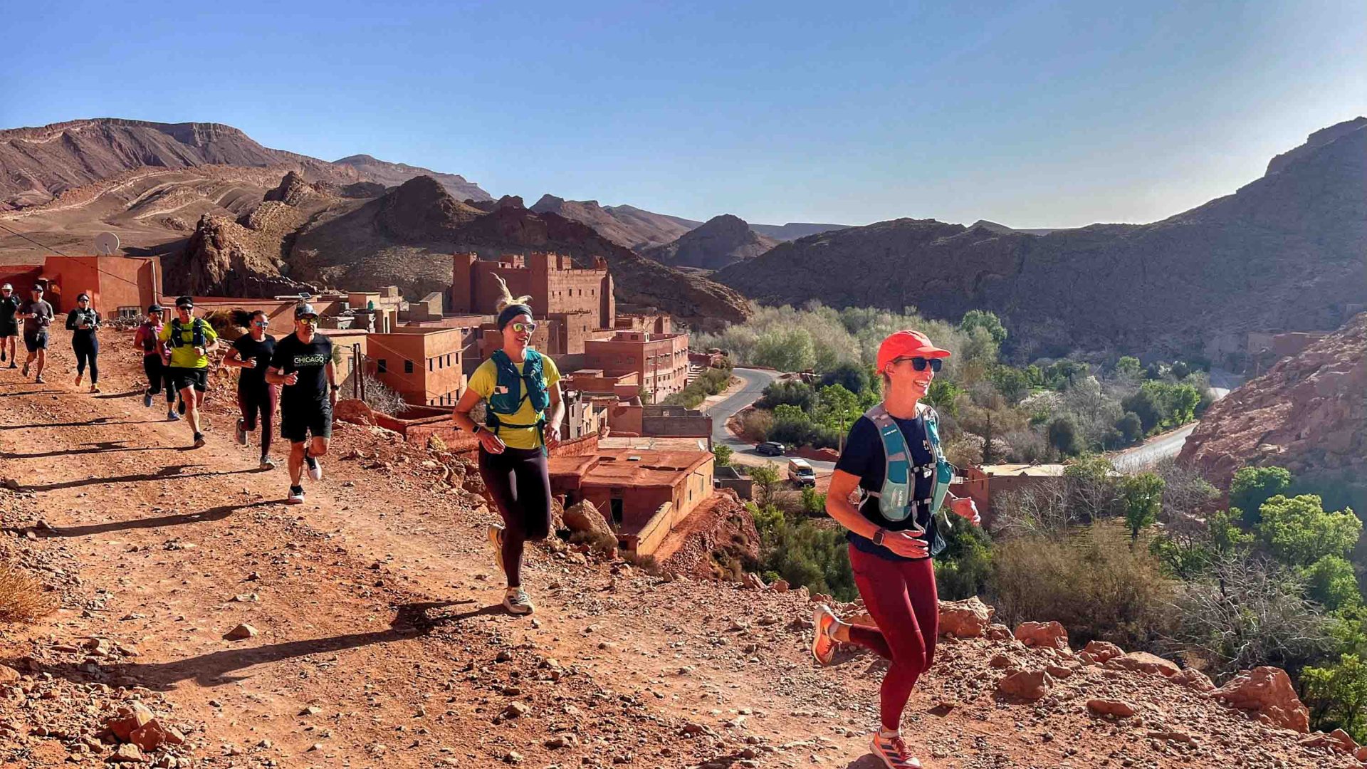 Runners on a dusty trail above a town in the hills.