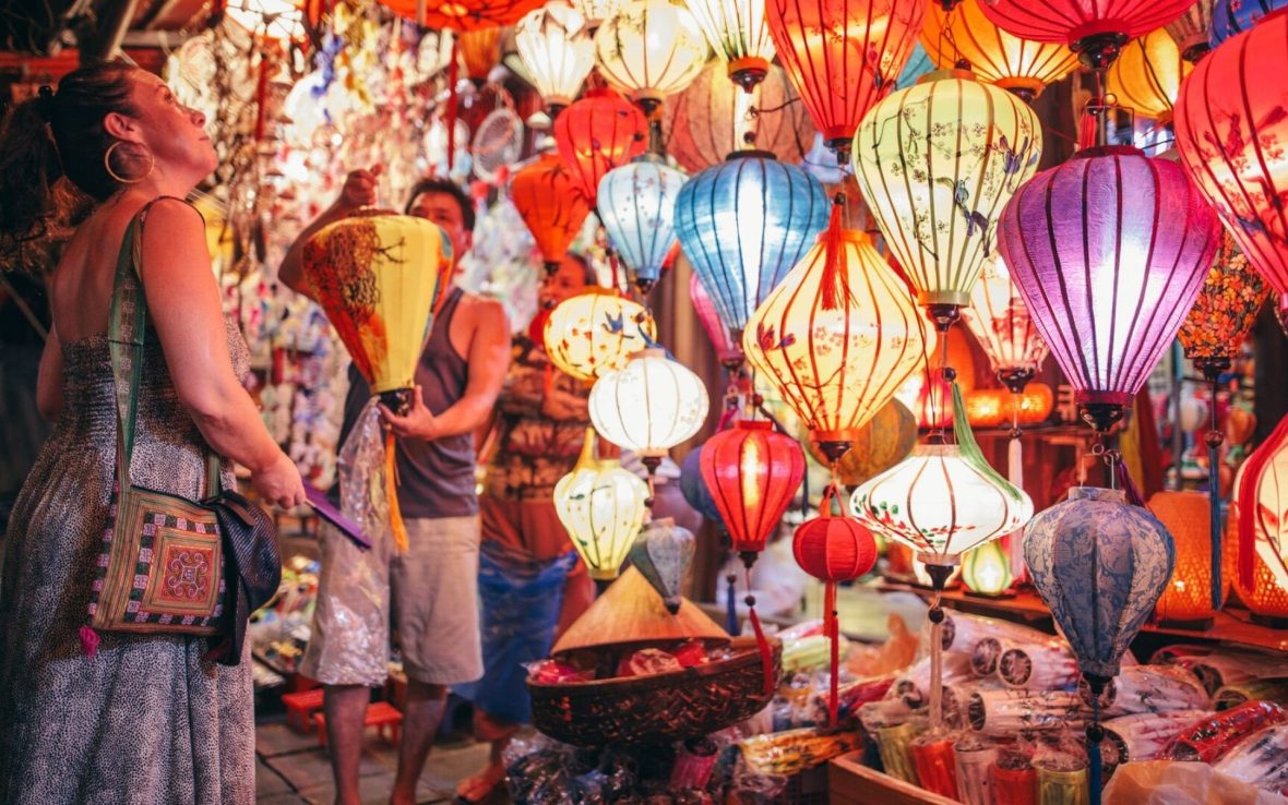 A woman wanders among traditional brightly colored lanterns in a shop.