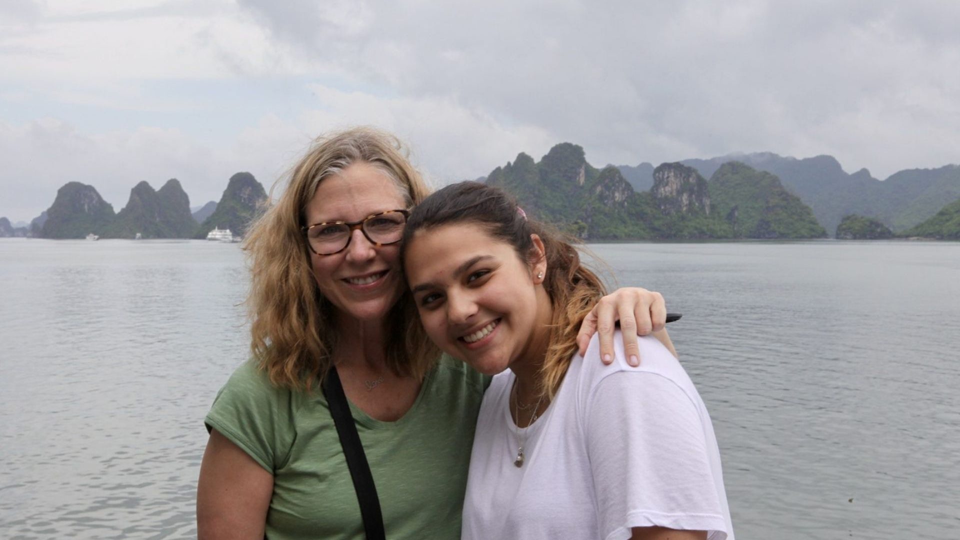 Two women, one with blonde hair and glasses, the other with dark hair, pose for a photo against Hạ Long Bay and its limestone karsts.