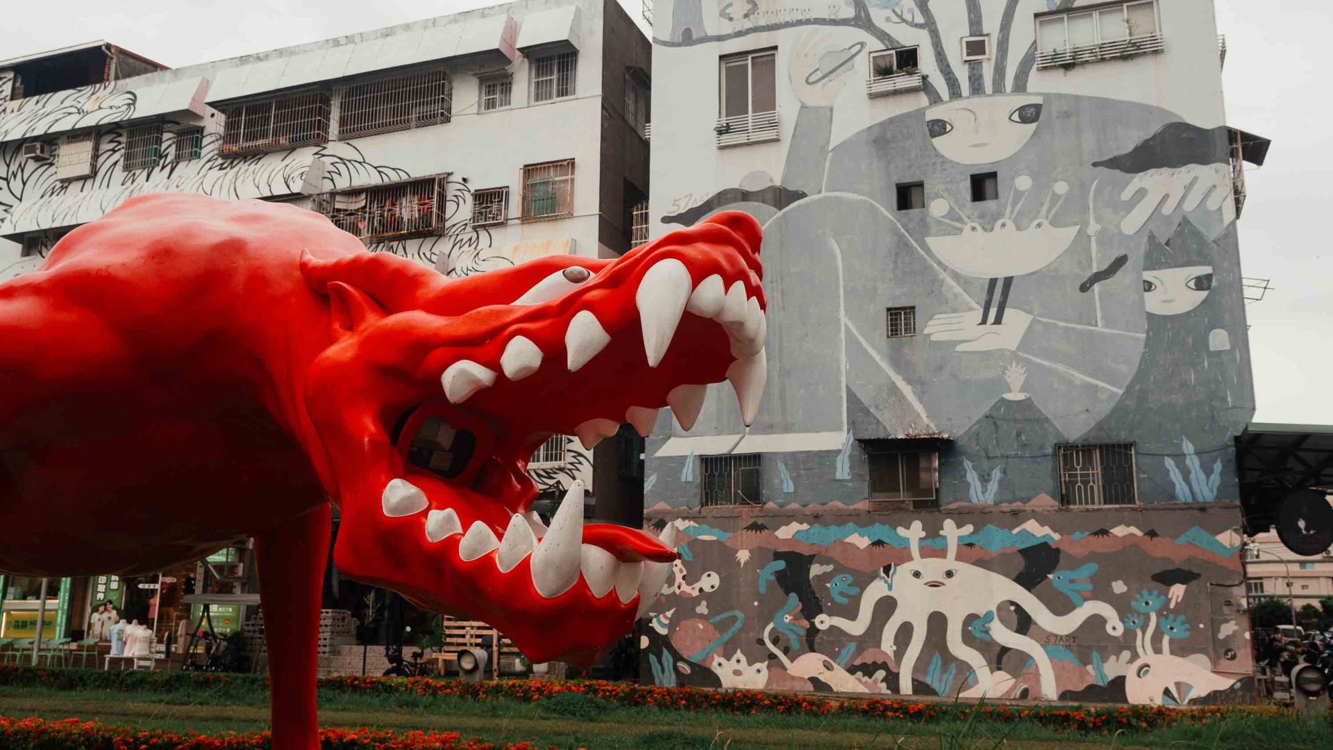 A red dragon sculpture in front of a wall with murals.