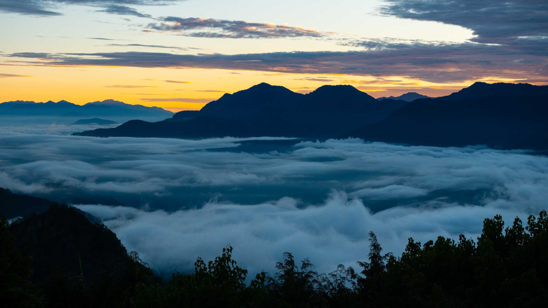 The sun rises over mountains. Clouds sit below the mountain summit, filling the valley.