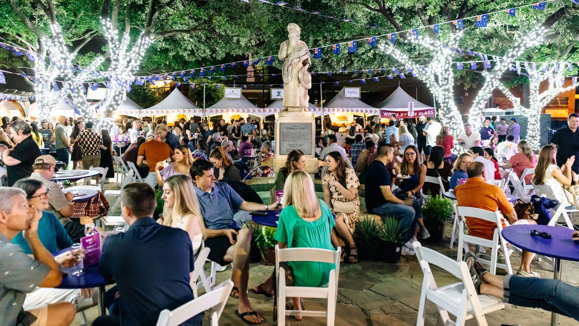 A busy plaza is filled with people drinking wine at night