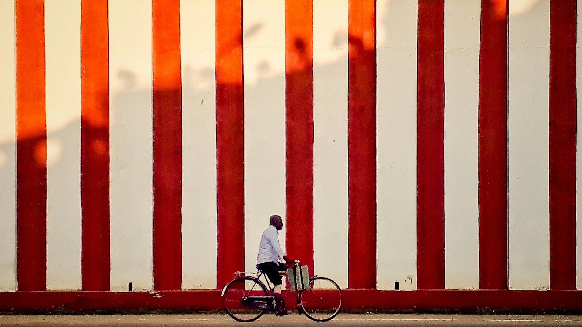 A man rides a bike infront of red and white striped wall.