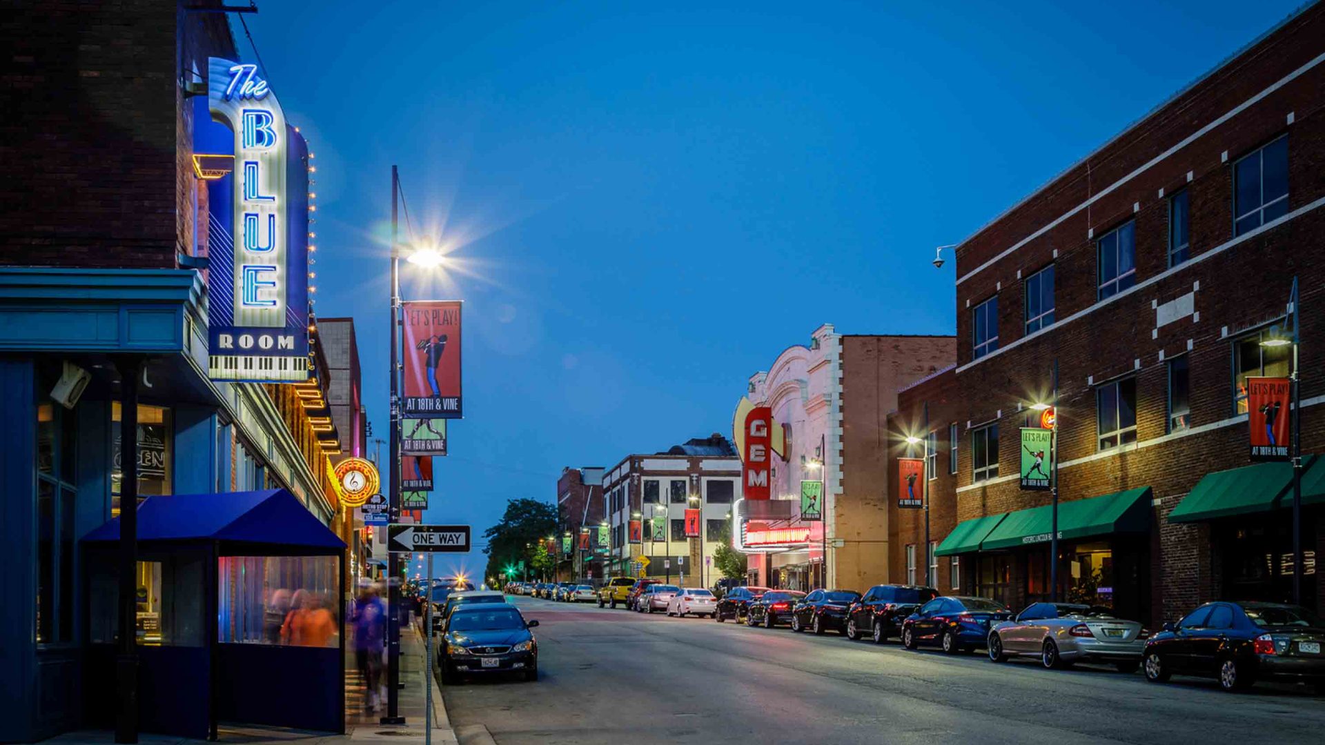 A nighttime streetscape with lit-up signs of various bars, restaurants and shops.