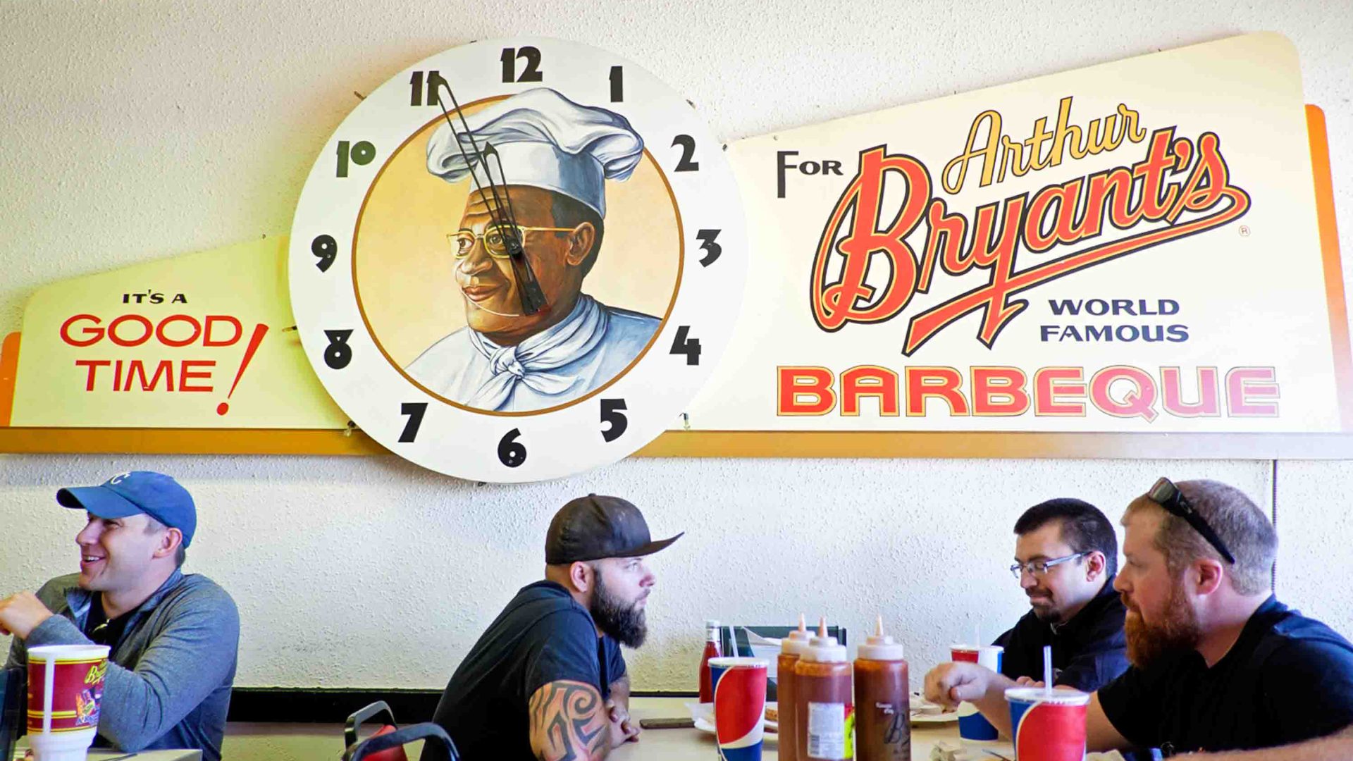 Men sit at a table talking below a retro sign for Arthur Bryant's World Famous Barbecue.