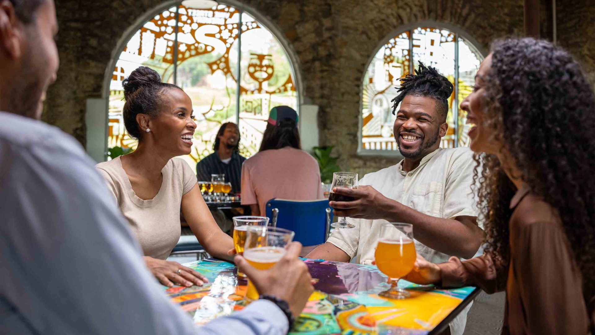 People laugh and smile around a table while eating and drinking.