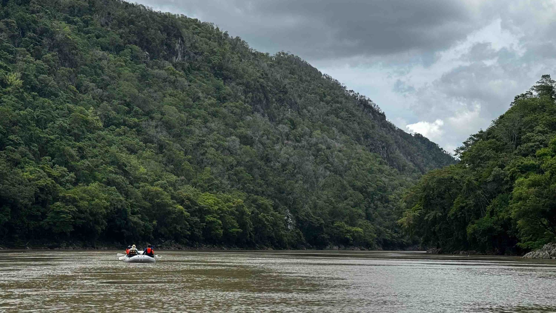 A small boat on a river with brown water, surrounded by lush greenery.