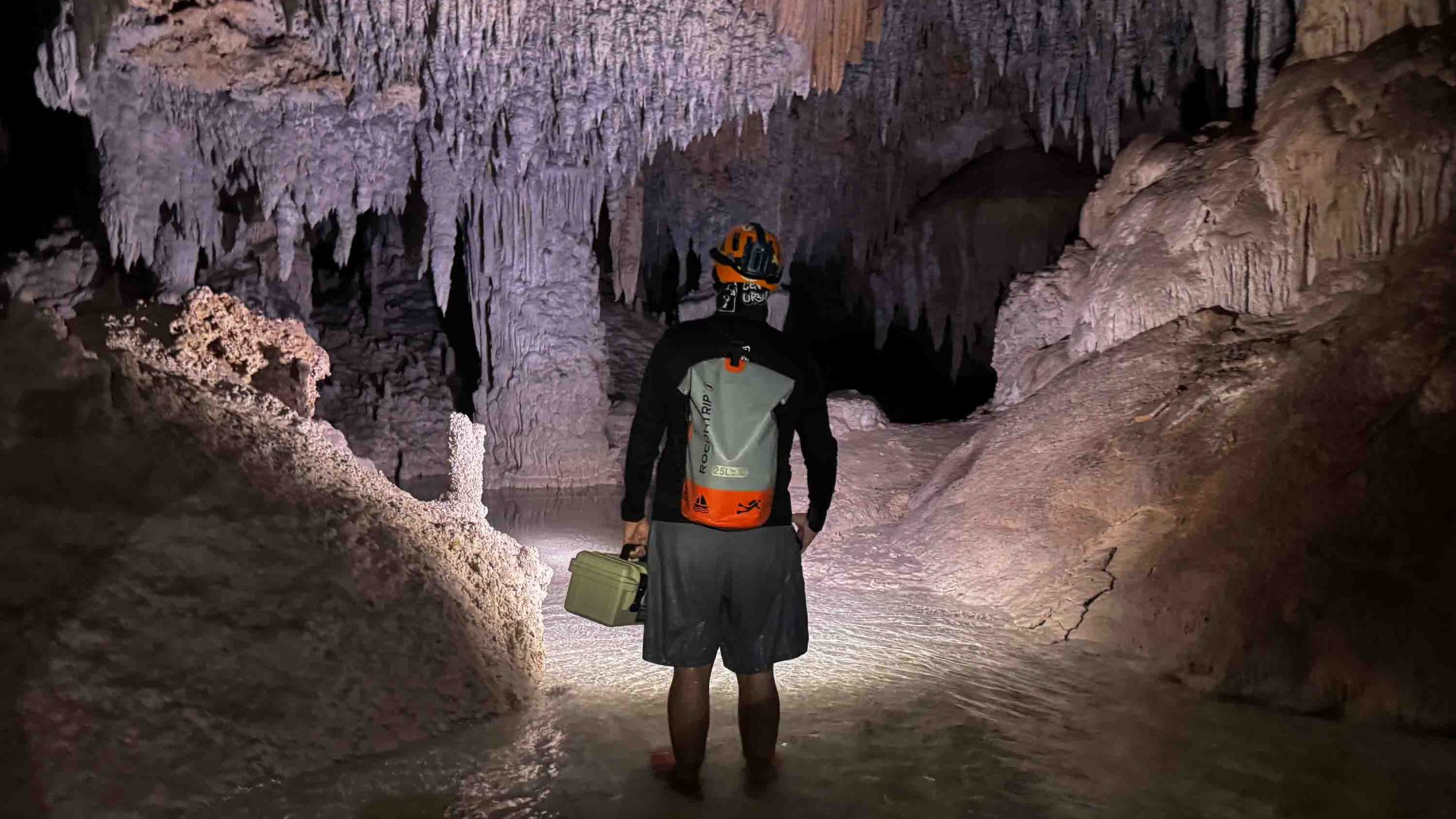 A man faces a cave with stalactites and water in it.